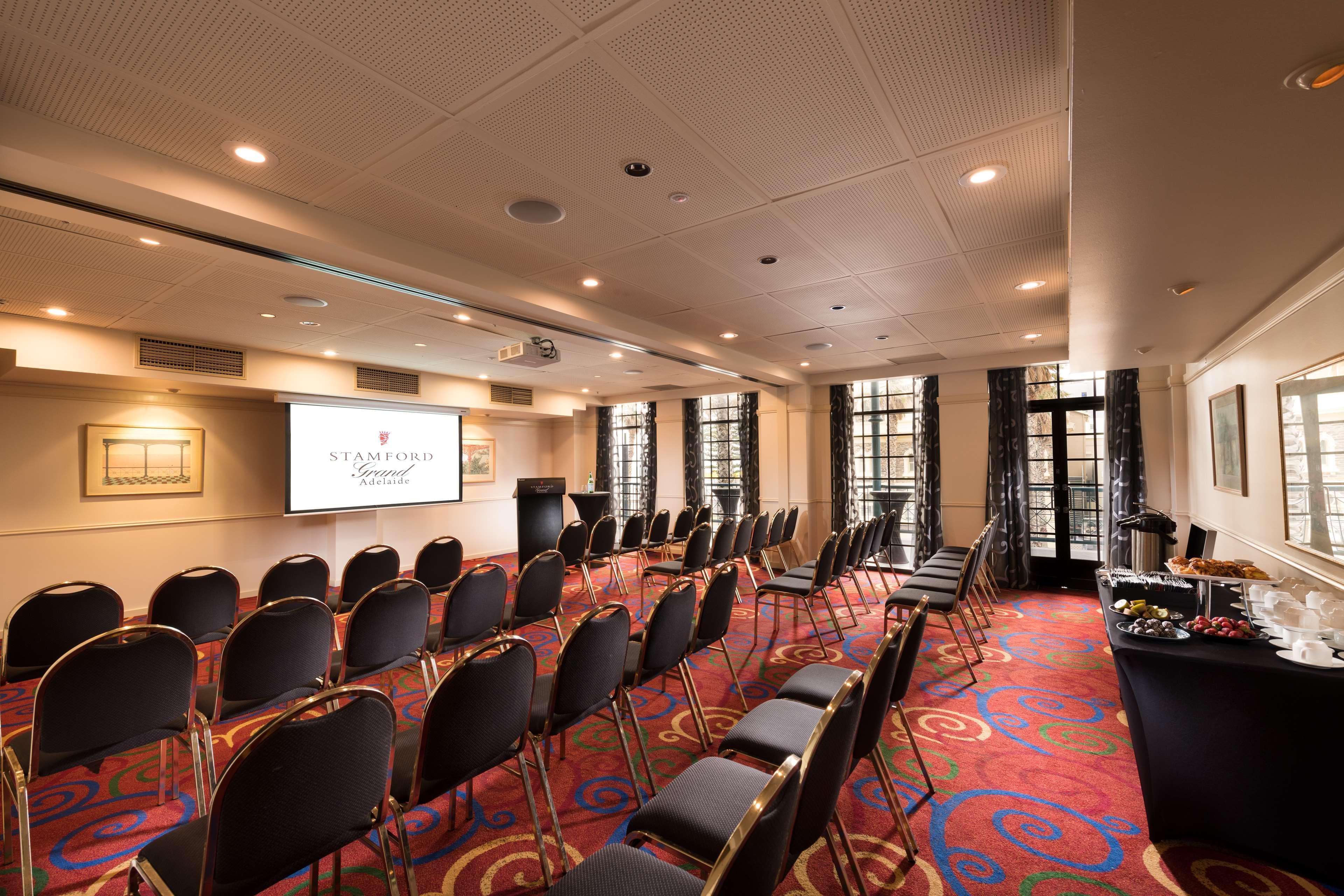 Stamford Grand Adelaide Hotel Glenelg Exterior foto The photo shows a conference room set up for an event. There are rows of black chairs arranged in a semicircular formation facing a presentation screen at the front. The room features large windows that allow natural light to enter, and the flooring 