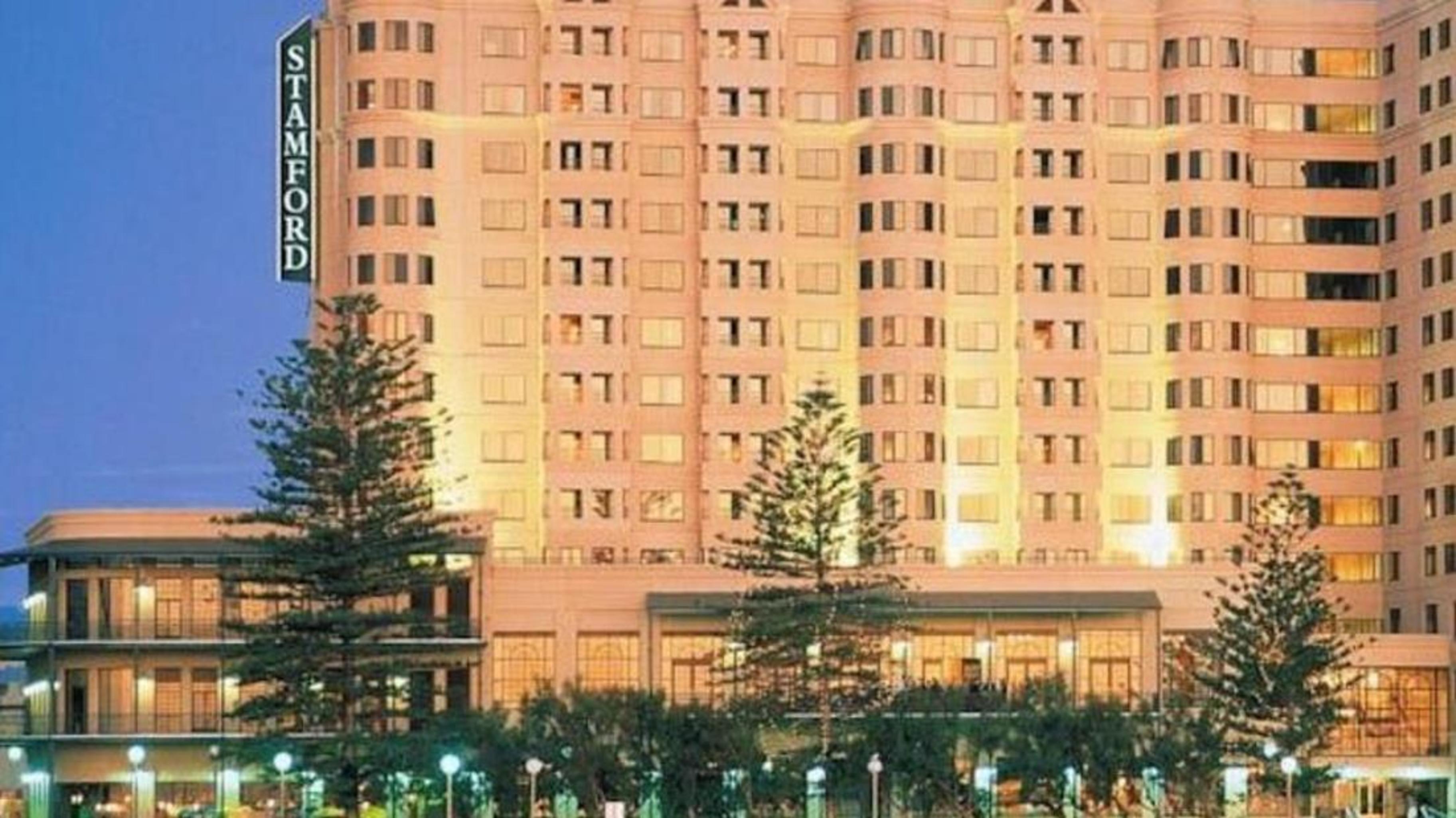 Stamford Grand Adelaide Hotel Glenelg Exterior foto The photo shows a tall, modern building illuminated at night, likely a hotel, with the name "Stamford" prominently displayed on its side. Surrounding the building are several palm trees and landscaped areas, suggesting a tropical or coastal location.