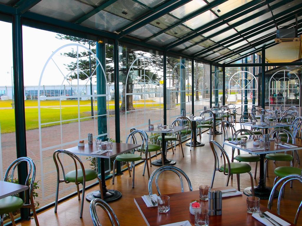 Stamford Grand Adelaide Hotel Glenelg Exterior foto The photo shows the interior of a restaurant with a modern design. The space features several tables with green chairs, arranged in a way that allows for ample seating. Large glass windows provide a view of the outside, creating a bright and open atm